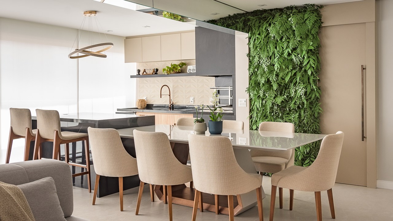 Paineis de porcelanato e jardim vertical revestem paredes em apê de 134 m². Projeto de Bianca Bahlis. Na foto, sala de jantar com jardim vertical e cadeiras estofadas. Varanda gourmet com churrasqueira.