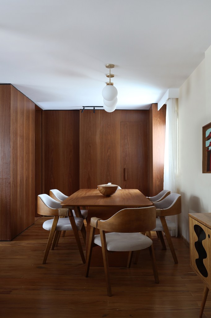 Peças retrôs e décor futurista se encontram no apartamento de 90 m². Projeto Trees Arquitetura. Na foto, sala de jantar com móveis e parede de madeira.