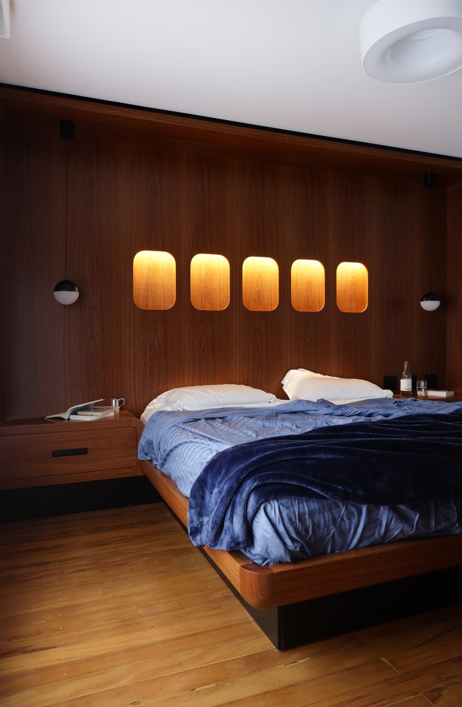 Peças retrôs e décor futurista se encontram no apartamento de 90 m². Projeto Trees Arquitetura. Na foto, quarto com parede de madeira e luminárias que parecem janelas.