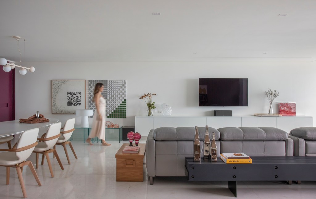 Sala de estar integrada com jantar com piso de mármore, sofá cinza e tv.