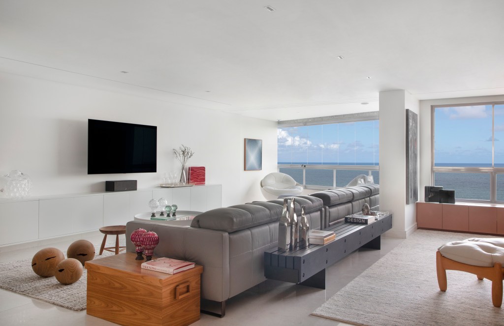 Sala de estar com piso de mármore branco, sofá cinza e vista para o mar.