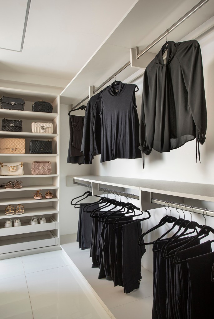 Closet com marcenaria branca e roupas pretas penduradas.