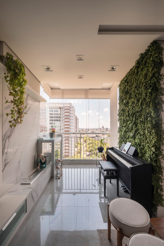 Ripas no teto e jardim vertical marcam a área social deste apê de 68 m². Projeto PB Arquitetura. Na foto, varanda com lareira e plantas. Piano e parede verde.