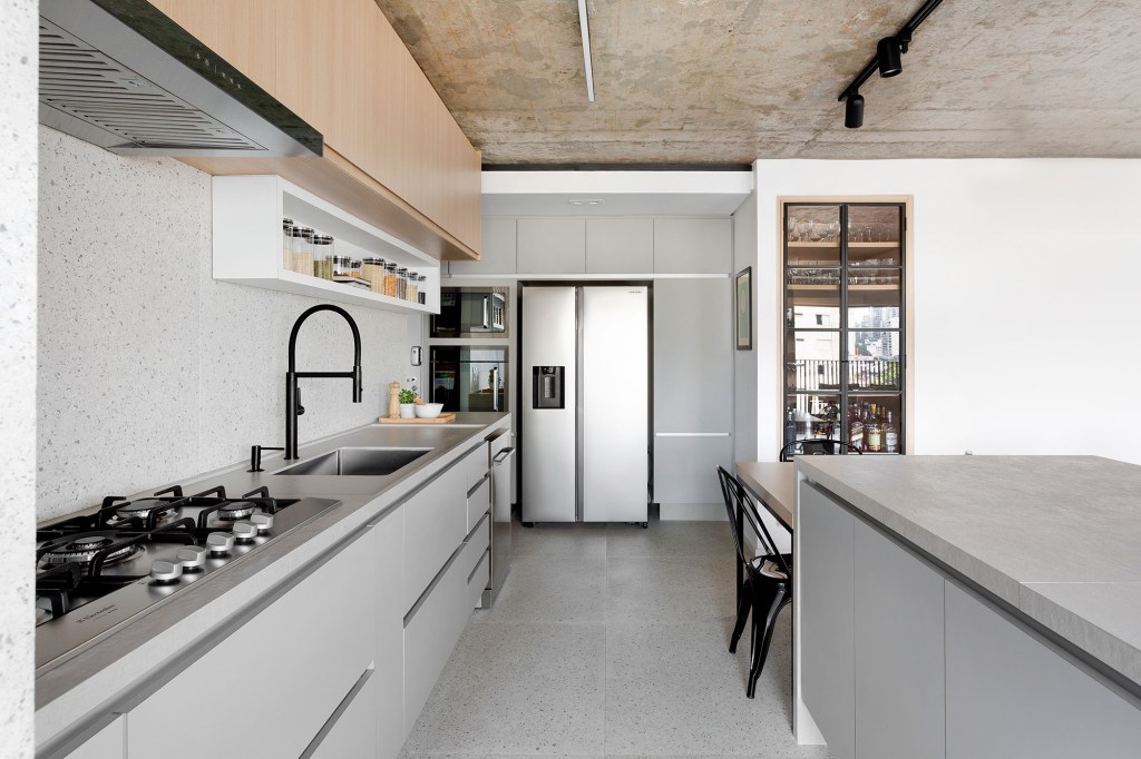 Apê de 142 m² ganha décor neutro que se integra aos eletrodomésticos. Projeto Degradê Arquitetura. Na foto, cozinha com bancada, mesa e parede com textura de granilite.