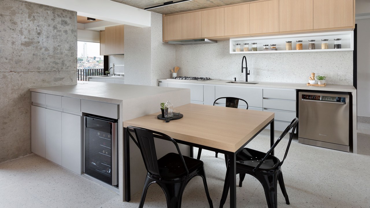 Apê de 142 m² ganha décor neutro que se integra aos eletrodomésticos. Projeto Degradê Arquitetura. Na foto, cozinha com bancada, mesa e parede com textura de granilite.