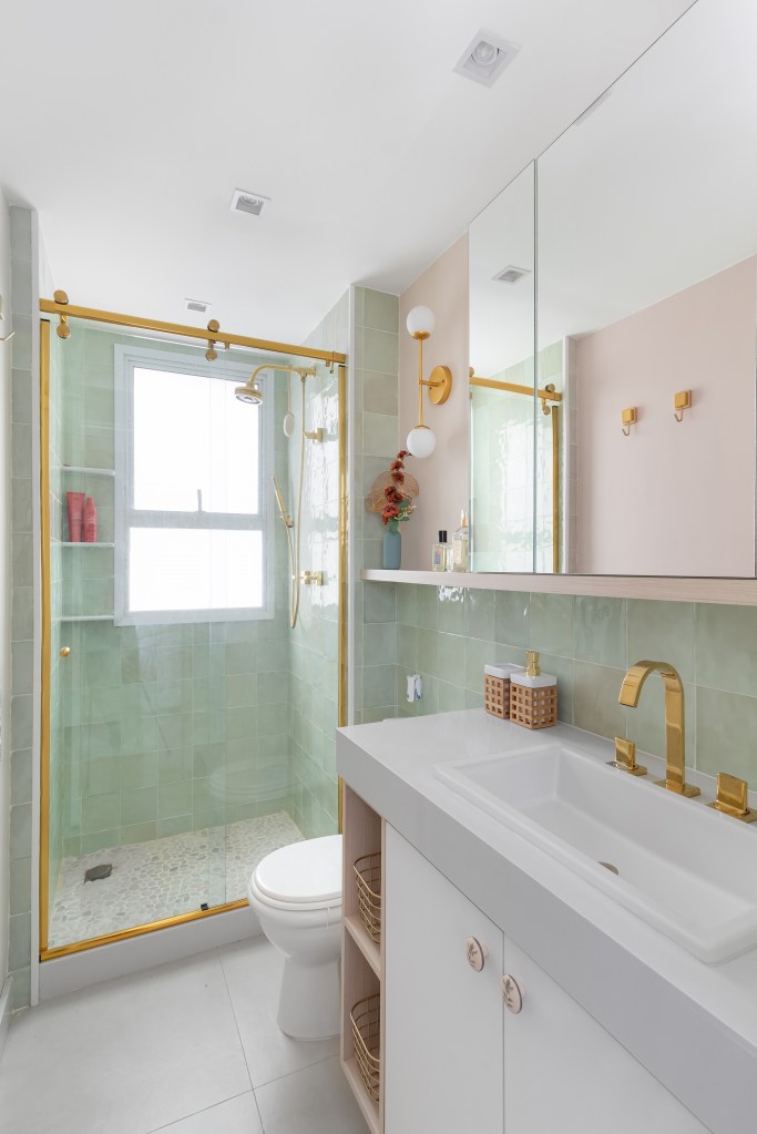 Apartamento colorido de 65 m² é cheio de referências ao pop art. Projeto de Pistache Arquitetura. Na foto, banheiro com metais dourados, parede verde e piso de seixos.