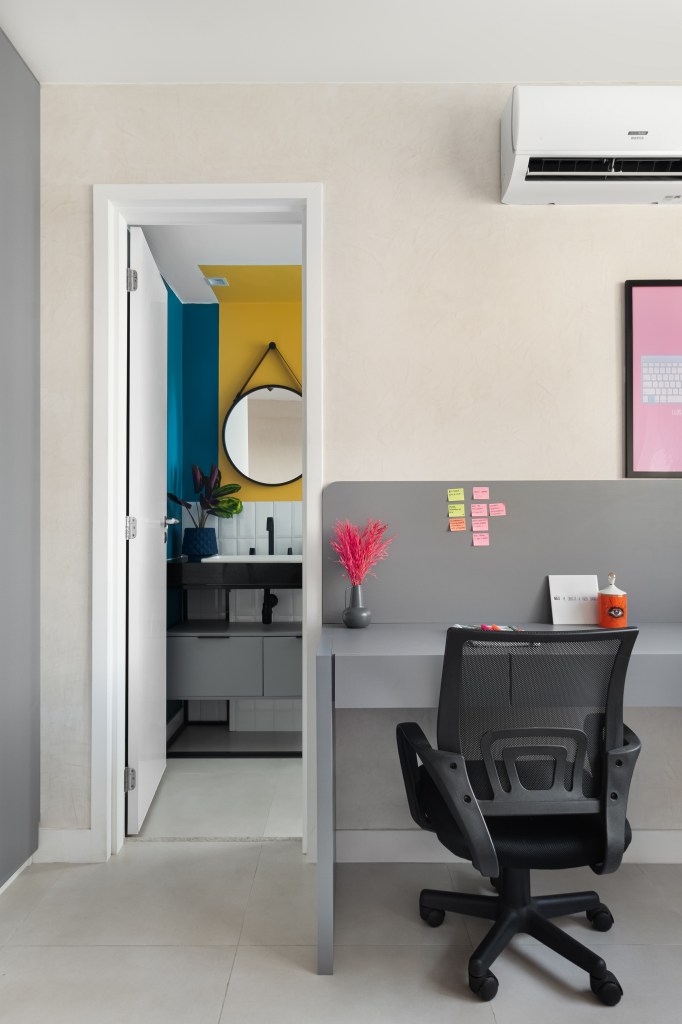 Apartamento colorido de 65 m² é cheio de referências ao pop art. Projeto de Pistache Arquitetura. Na foto, escritório com bancada cinza, Banheiro com parede amarela e azul e espelho redondo.