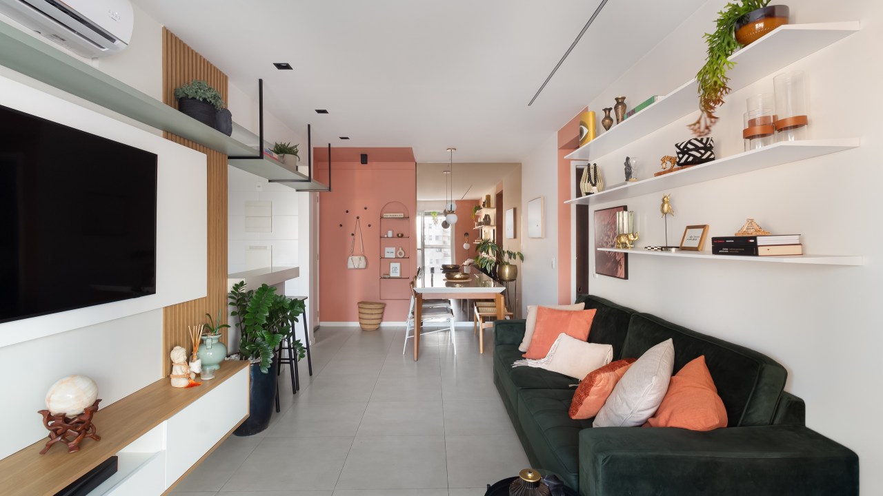 Apartamento colorido de 65 m² é cheio de referências ao pop art. Projeto de Pistache Arquitetura. Na foto, sala integrada com o jantar, parede rosa, tv, ripado e prateleiras.
