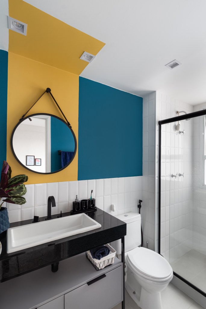 Apartamento colorido de 65 m² é cheio de referências ao pop art. Projeto de Pistache Arquitetura. Banheiro com espelho redondo, parede azul e amarela.