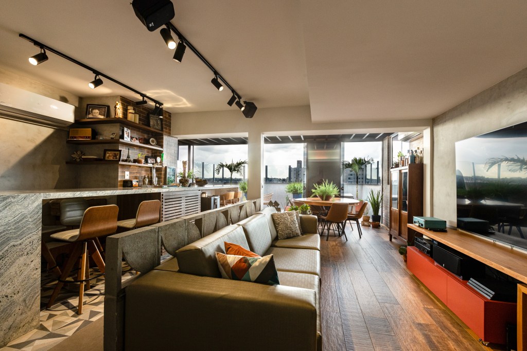 Sala de estar integrada com jantar e cozinha, rack de madeira e iluminação com trilho de spot.