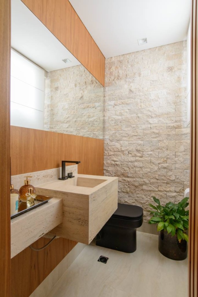 Apê de 140 m² feito para receber une madeira e mármore no décor. Projeto de Letícia Nannetti. Na foto, banheiro com pedra na parede, madeira e espelho.