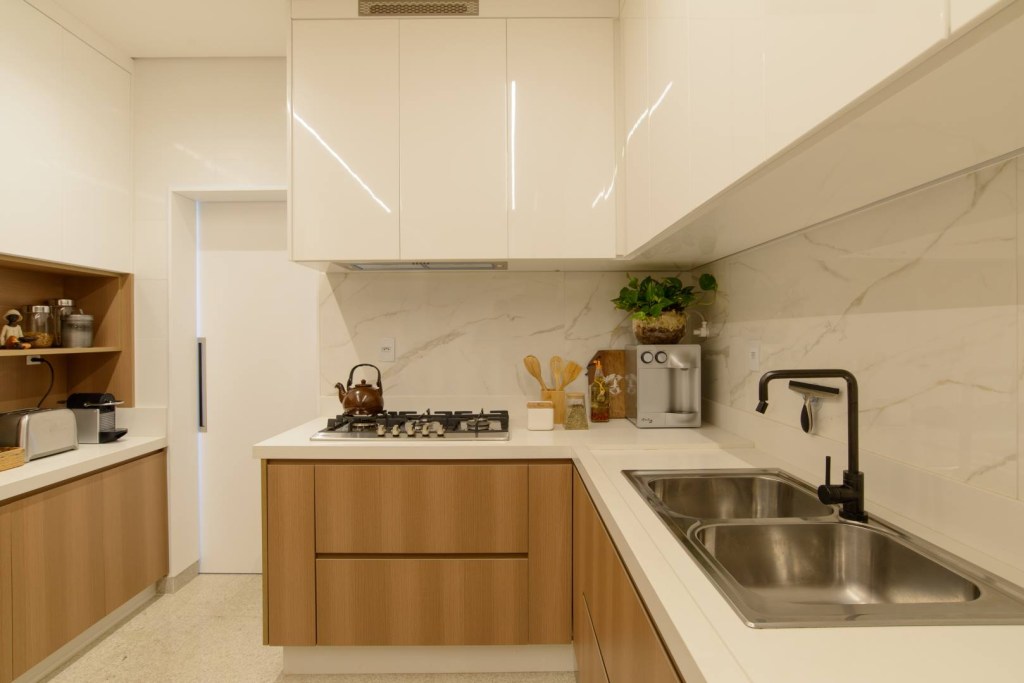 Apê de 140 m² feito para receber une madeira e mármore no décor. Projeto de Letícia Nannetti. Na foto, cozinha com armarios de madeira e tampo branco.
