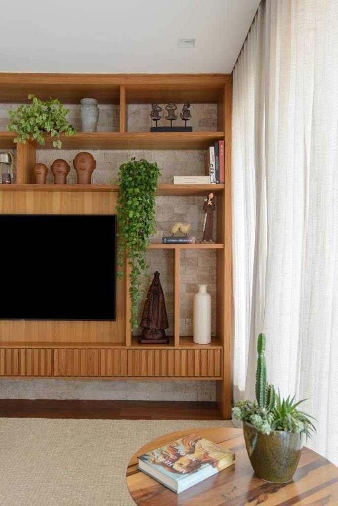 Apê de 140 m² feito para receber une madeira e mármore no décor. Projeto de Letícia Nannetti. Na foto, sala de estar com varanda, estante e parede de pedra.
