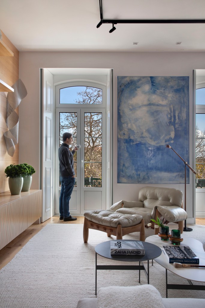 Sala de estar com janela, quadro azul, poltrona mole e luminária de piso.