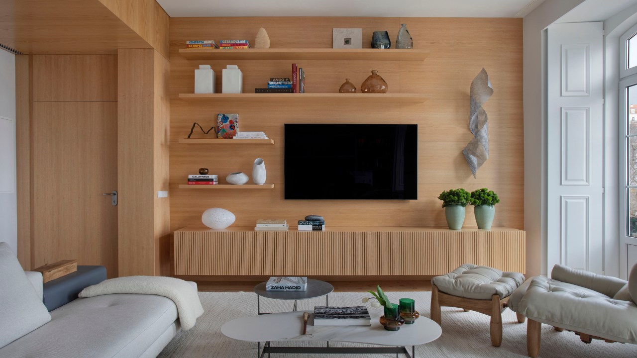 Sala de estar; sala de tv com parede revestida de madeira, rack de madeira, prateleiras, tv, tapete branco, sofá branco e poltrona mole.