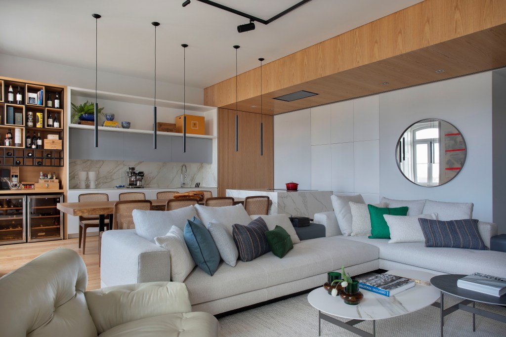 Sala de estar integrada com cozinha com sofá branco, almofadas pequenas azuis, mesa de centro com tampo de mármore.