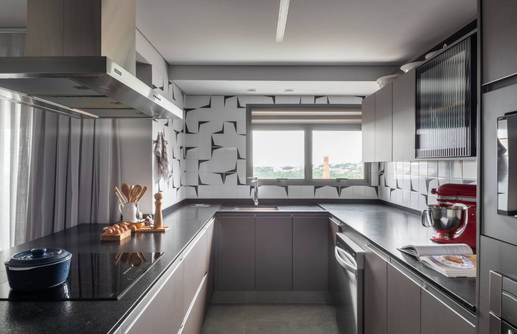 ape-155m-paleta-de-cores-sobria-cozinha-forma-u-sotaque-arquitetura-05 Cozinha em formato de u com janela, bancada preta, armários taupe e parede de azulejos.
