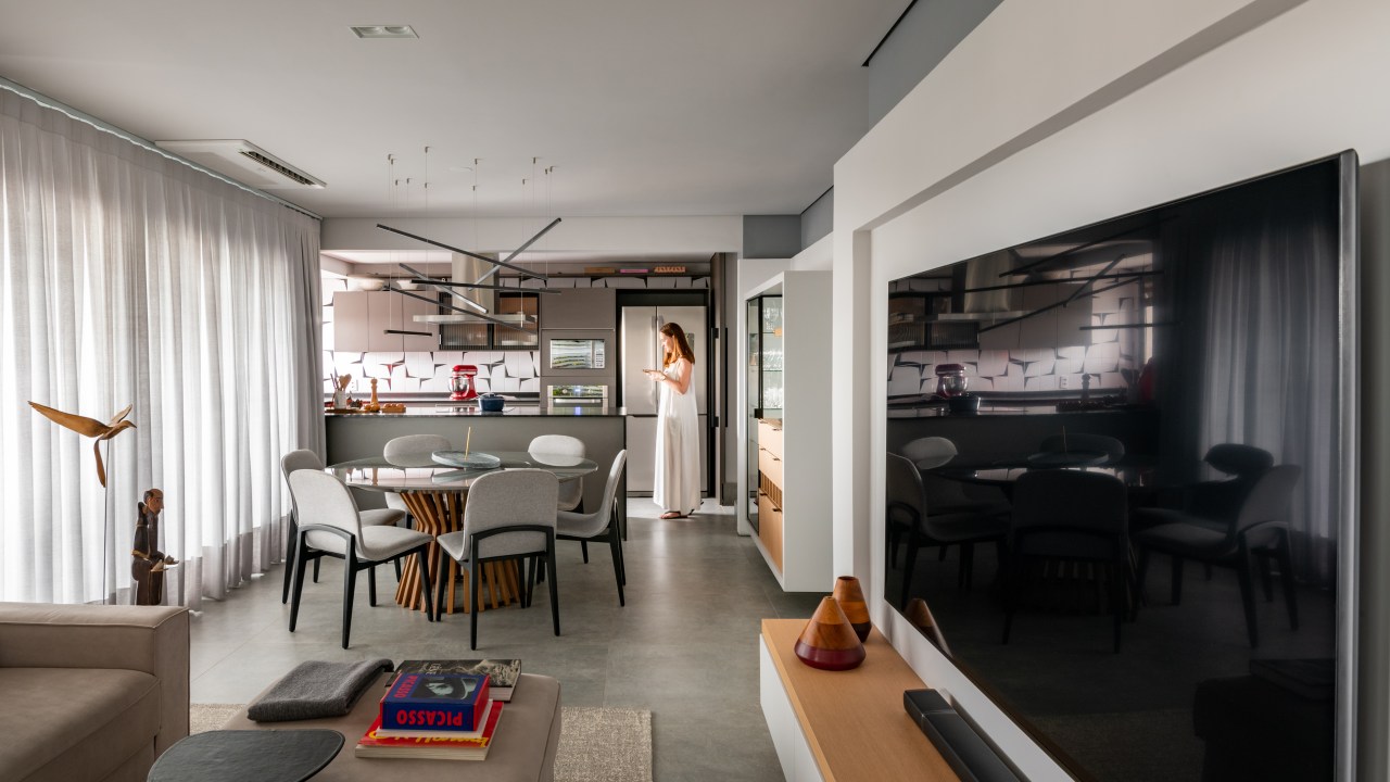 Sala de tv integrada com jantar e cozinha com piso de porcelanato cinza e mesa redonda.