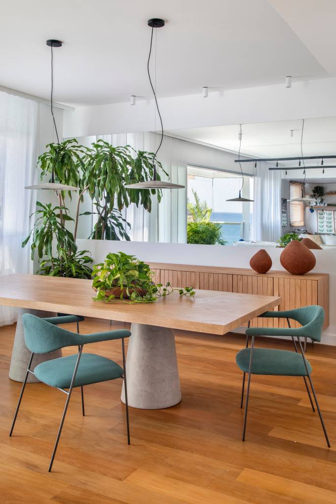 Sala de jantar com espelho, mesa de madeira e cadeiras verdes.