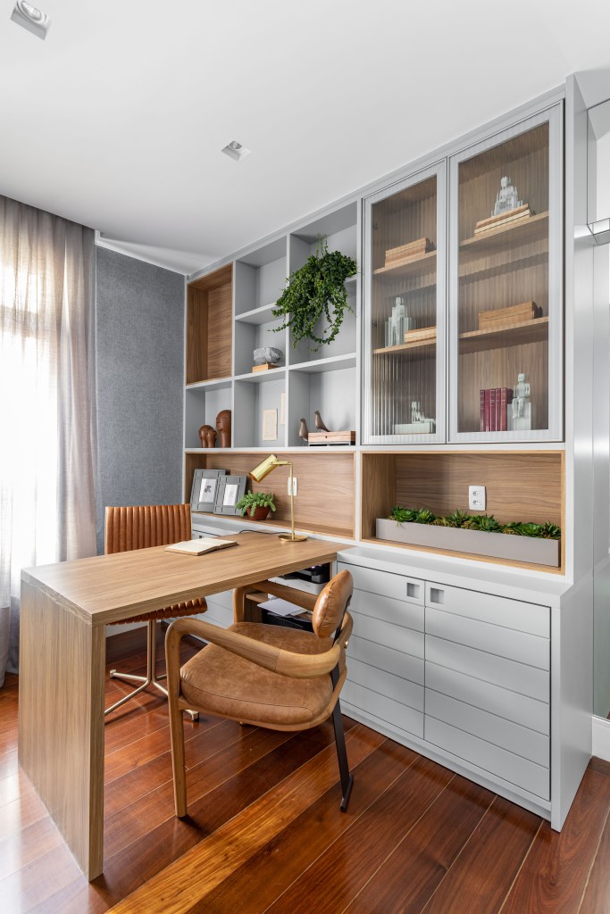 Home office com bancada de madeira embutida em armário com portas de vidro.