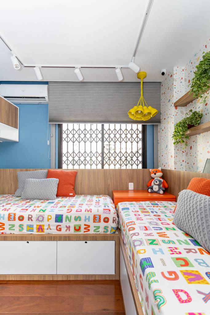 Quarto infantil com duas camas de solteiro com roupa de cama colorida e parede azul.