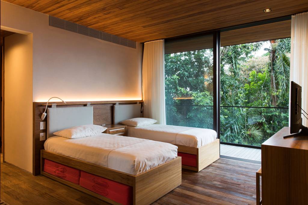 Casa de 153 m² se camufla em meio à natureza do litoral paulista. Projeto de Daniel Fromer, interiores de Julyana Bortolotto. Na foto, quarto com vista para a mata e forro de madeira.