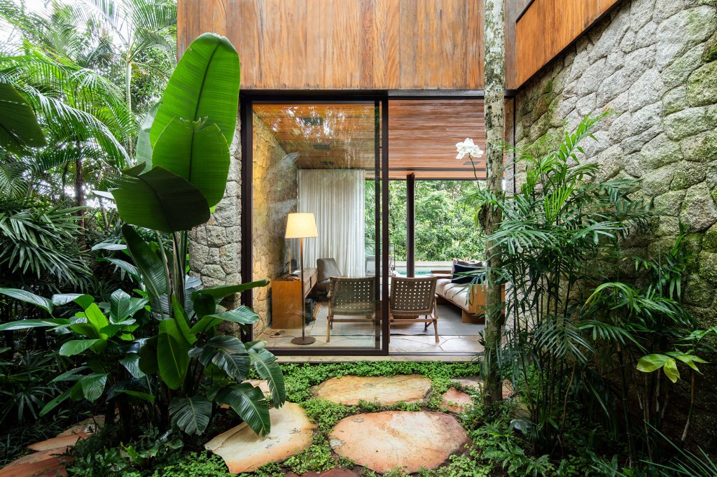 Casa de 153 m² se camufla em meio à natureza do litoral paulista. Projeto de Daniel Fromer, interiores de Julyana Bortolotto. Na foto, sala de estar com parede de vidro.