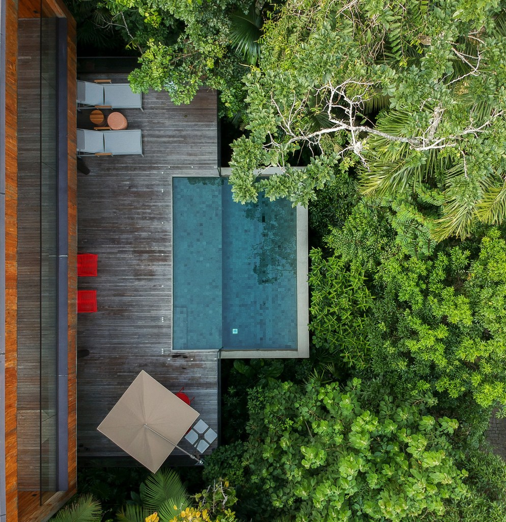 Casa de 153 m² se camufla em meio à natureza do litoral paulista. Projeto de Daniel Fromer, interiores de Julyana Bortolotto. Na foto, vista áerea da piscina no meio da mata.
