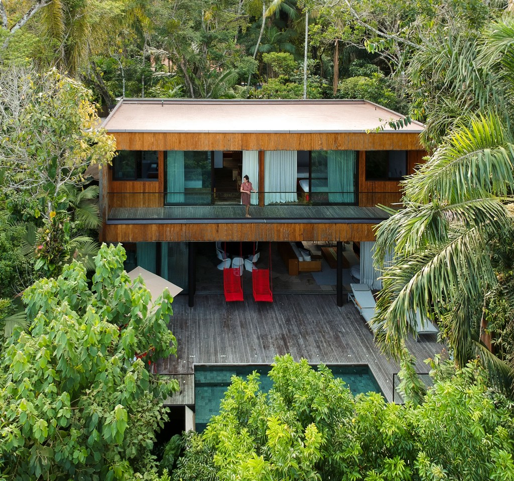 Casa de 153 m² se camufla em meio à natureza do litoral paulista. Projeto de Daniel Fromer, interiores de Julyana Bortolotto. Na foto, fachada com varandas dos quartos e piscina.