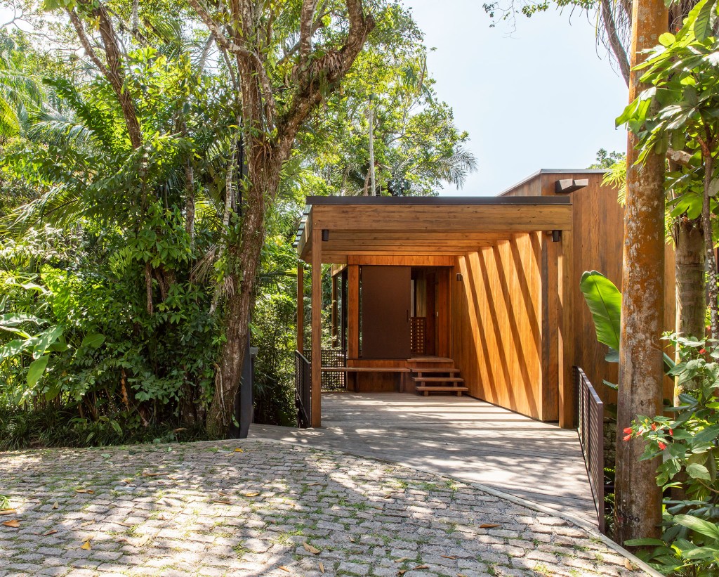 Casa de 153 m² se camufla em meio à natureza do litoral paulista. Projeto de Daniel Fromer, interiores de Julyana Bortolotto. Na foto, entrada da casa com pergolado e vista para o jardim.