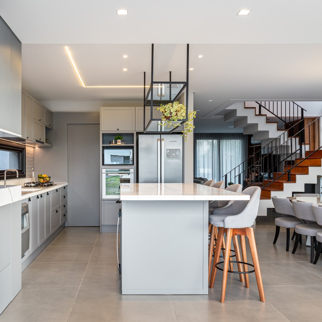 Cozinha integrada com ilha de quartzo branco, banquetas cinza, armários cinza em estilo provençal.