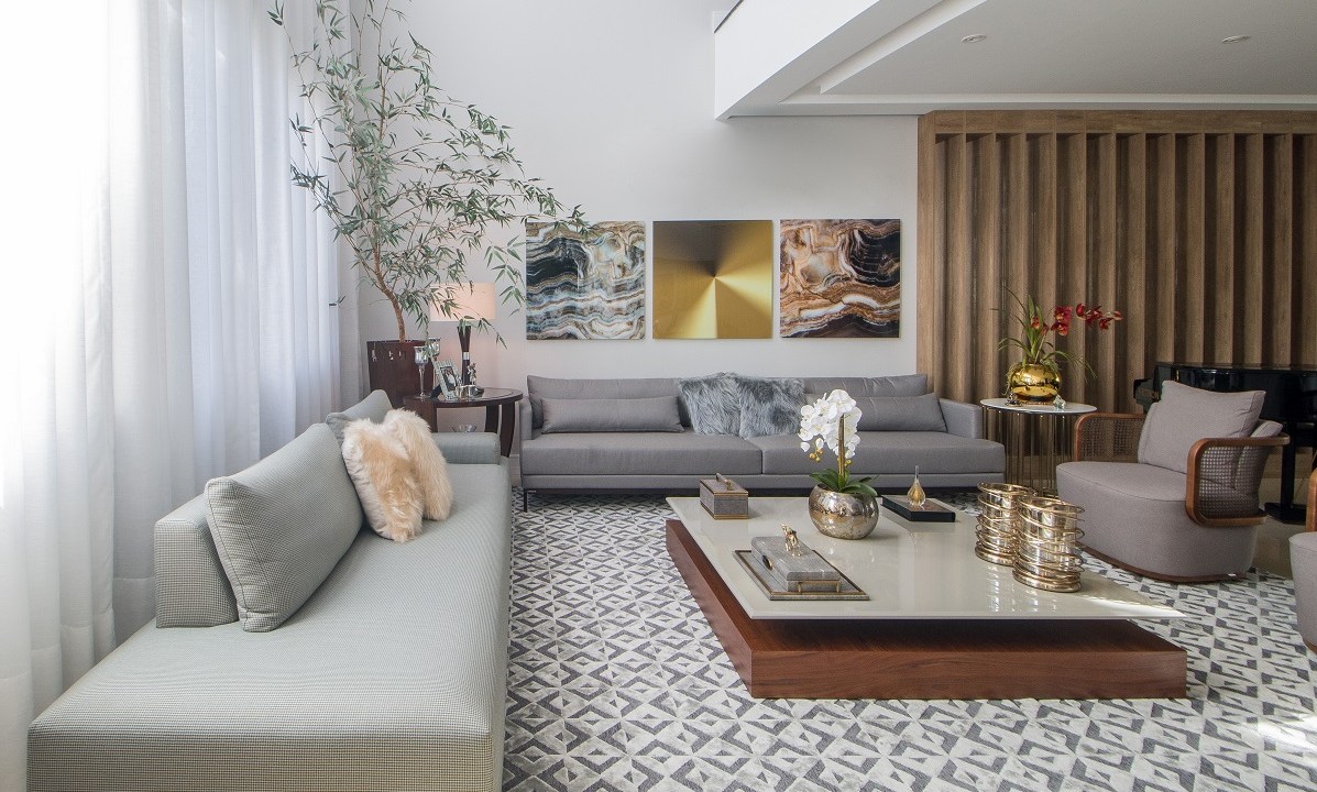 Casa de 500 m² possui detalhes dourados em todos os ambientes. Projeto de Ana Cano Milman. Na foto, sala de estar com sofá cinza, piano, tapete e mezanino.
