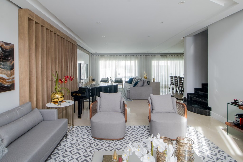 Casa de 500 m² possui detalhes dourados em todos os ambientes. Projeto de Ana Cano Milman. Na foto, sala de estar com poltronas, sofá e piano.
