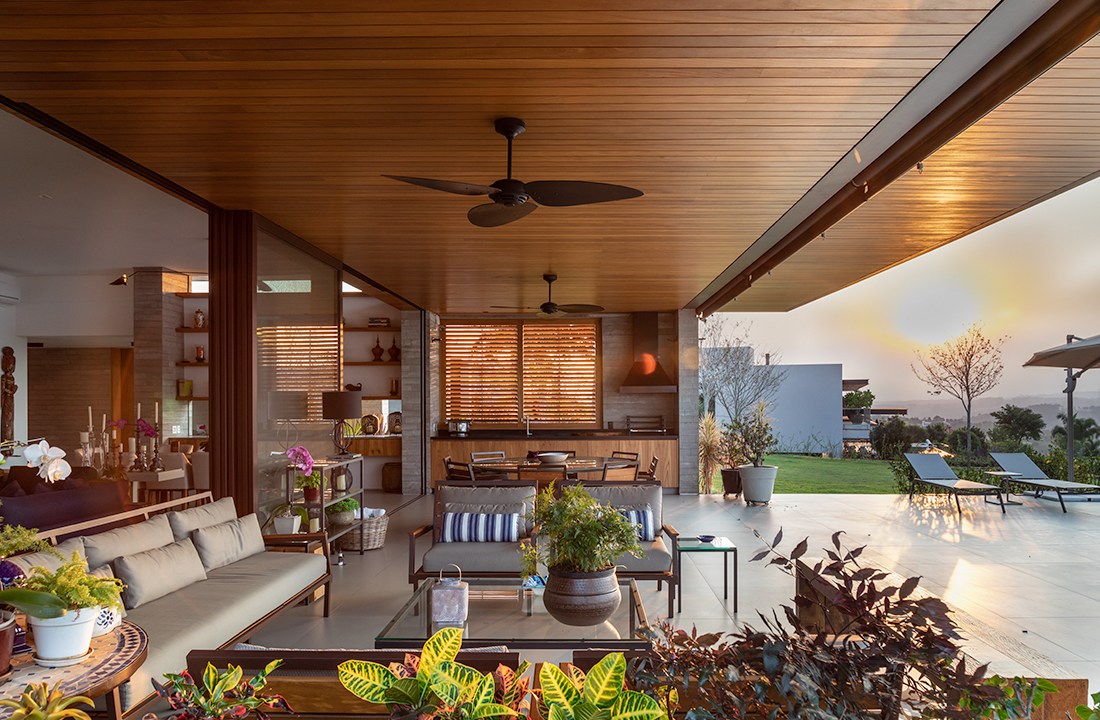 Casa de campo térrea tem vista para o laranjal e espaço para shuffleboard. Projeto de Gilda Meirelles. Na foto, varanda aberta para o jardim com estar e gourmet.