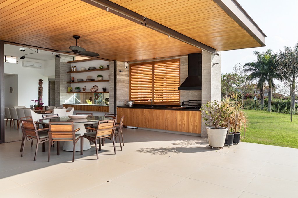 Casa de campo térrea tem vista para o laranjal e espaço para shuffleboard. Projeto de Gilda Meirelles. Na foto, varanda aberta para o jardim com estar e gourmet.
