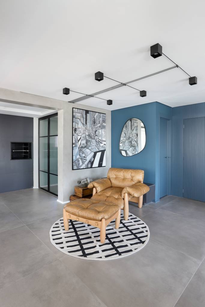 Sala de estar com piso de porcelanato cimento queimado, poltrona mole e tapete preto e branco.