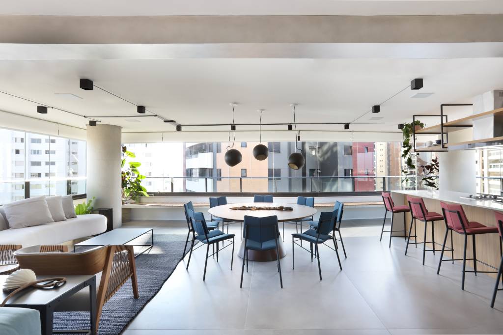 Sala de estar, varanda e jantar integradas com piso de porcelanato cimento queimado e mesa redonda com cadeiras azuis.