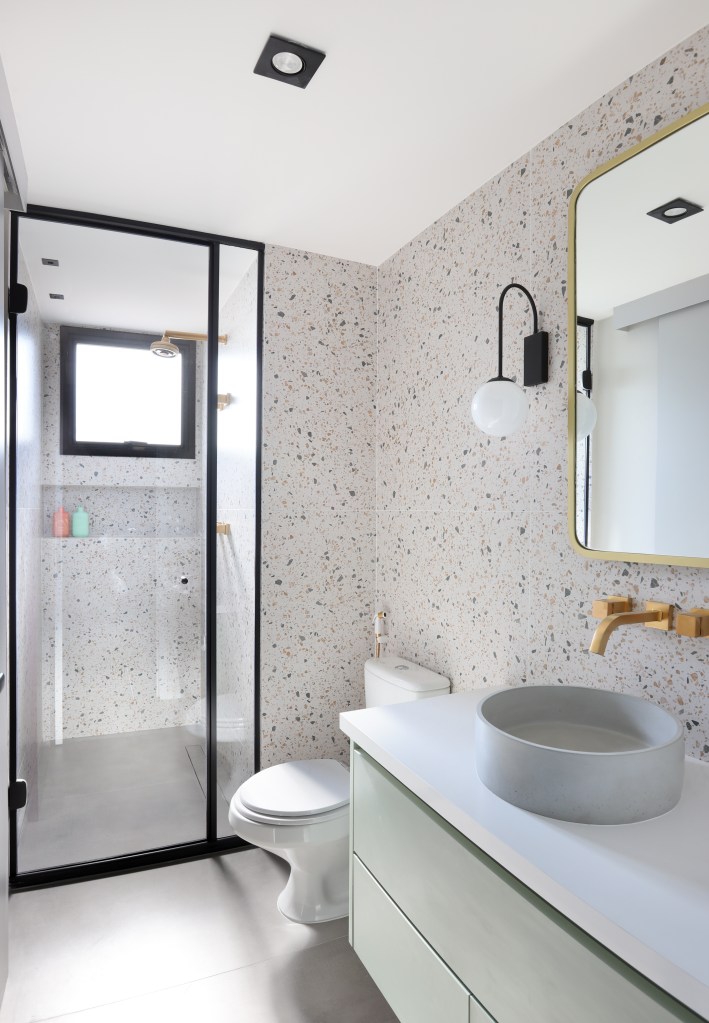Banheiro com cuba solta, papel de parede e arandelas ao lado do espelho.