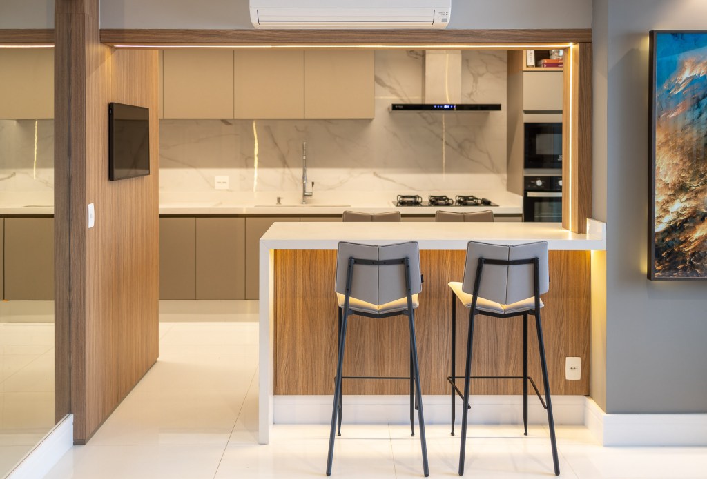 Cozinha integrada com bancada branca e banquetas de madeira.
