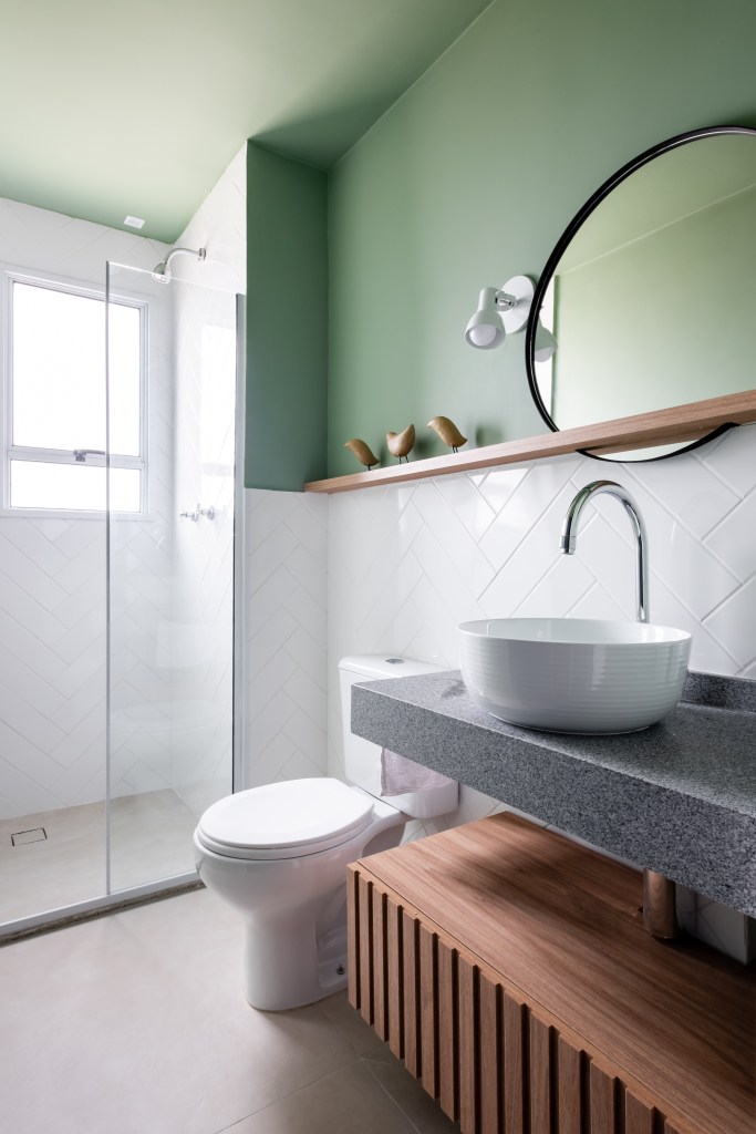 Banheiro com meia parede verde, parede de azulejos brancos e cuba solta branca.