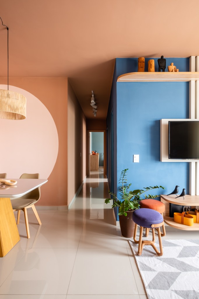 Sala de estar integrada com jantar, parede rosa e azul, mesa de jantar pequena.