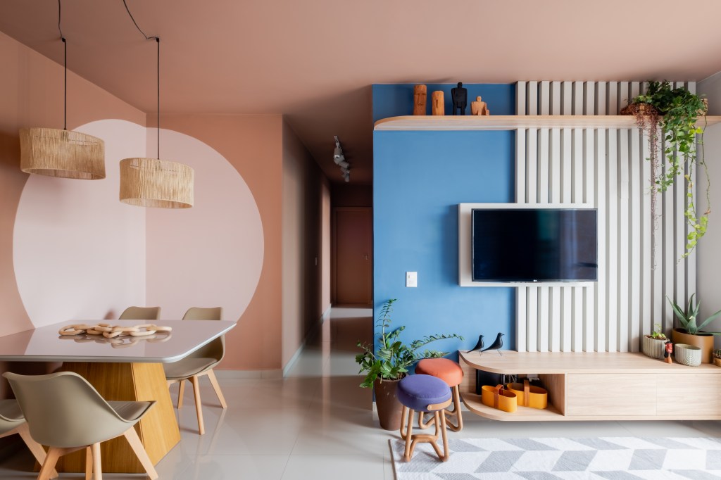 Sala de estar integrada com jantar, parede rosa e azul, mesa de jantar pequena.