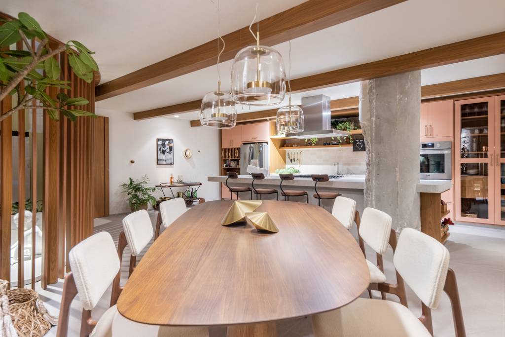 Cozinha une marcenaria rosa, brises, horta e granito branco. Projeto de Bruno Moraes para a CASACOR SP 2023. Na foto, cozinha e sala de jantar com mesa de madeira, parede de brise e pilar aparente.