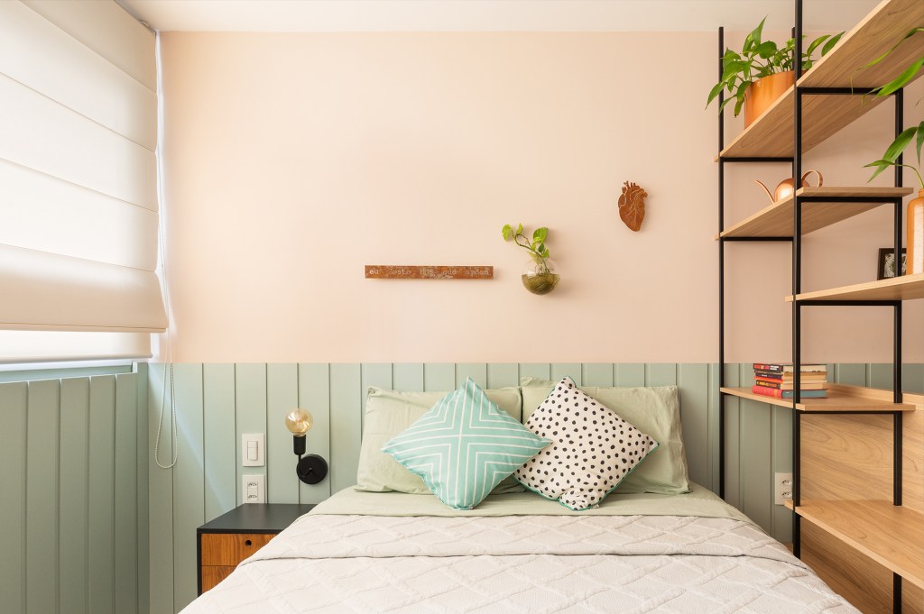 Estante de serralheria separa quarto e cozinha neste apê de 23 m². Projeto do Estúdio Taco. Na foto, quarto de casal com lambri na cabeceira e décor verde e rosa.