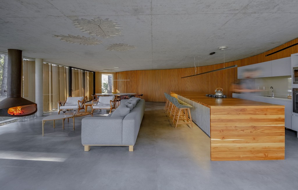 Layout minimalista marca casa térrea de 201 m² no Rio Grande do Sul. Projeto de Stemmer Rodrigues Arquitetura. Na foto, sala de estar com cozinha integrada, parede de brise e lareira.