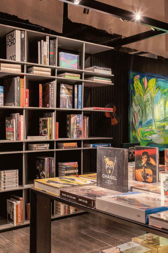 Esta livraria tem clima intimista e repleta de arte brasileira. Projeto de Nana Cunha, Caru Cunha e Sílvia Camargo para a CASACOR SP 2023. Na foto, estantes com livros, paredes escuras e quadros.