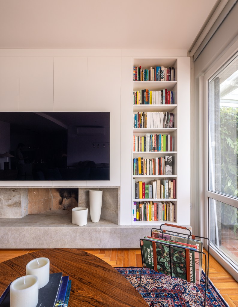 Sala de tv com painel branco e estante de livros.