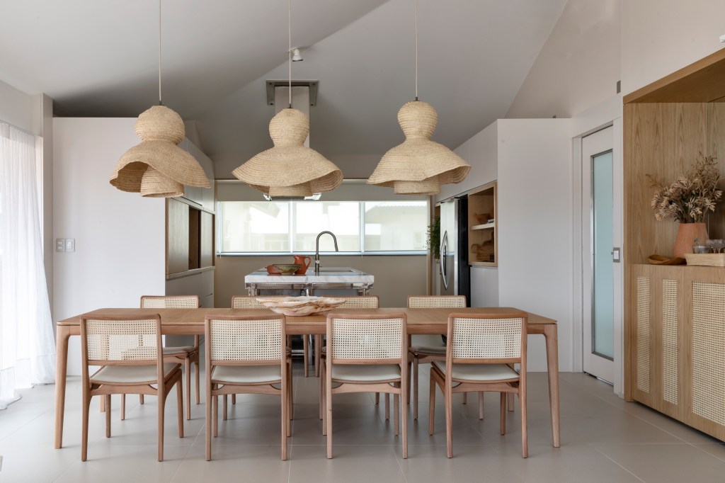 Sala de jantar integrada com cozinha com mesa de madeira e luminárias de palhinha.
