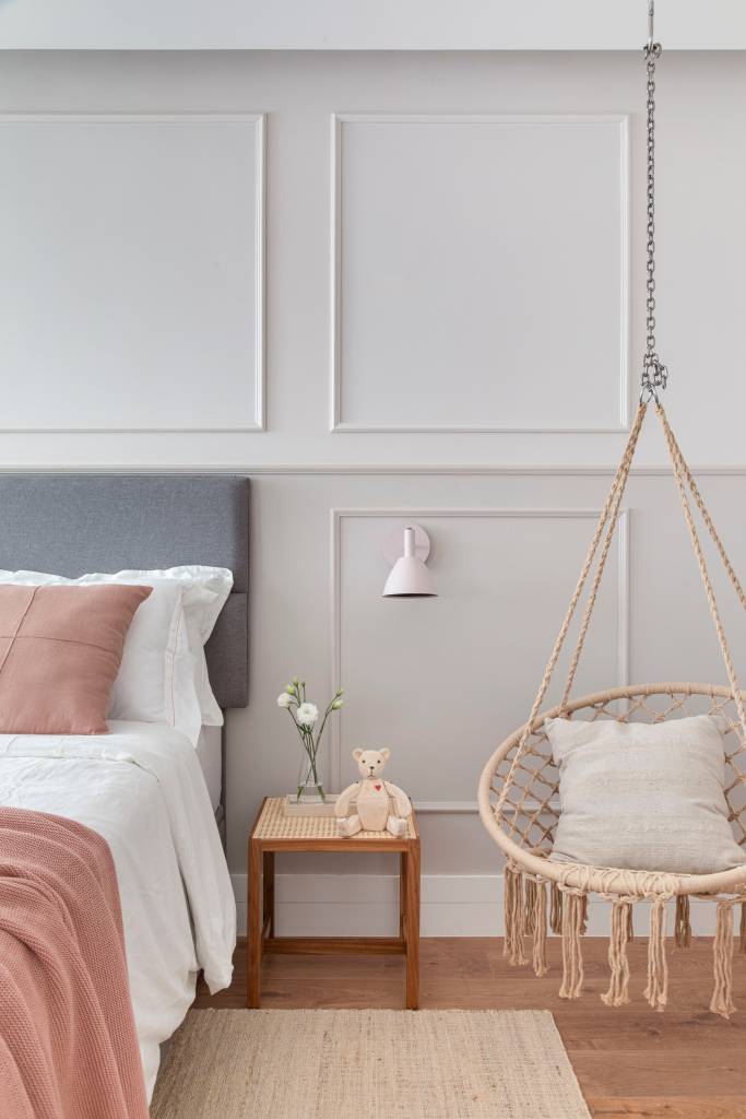 Quarto infantil de menina com penteadeira, parede com lambris e boiseries, cabeceira estofada e balanço.
