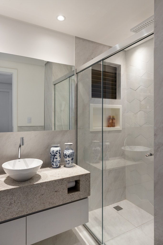 Banheiro pequeno com armário cinza e armário aéreo espelhado com prateleiras brancas.